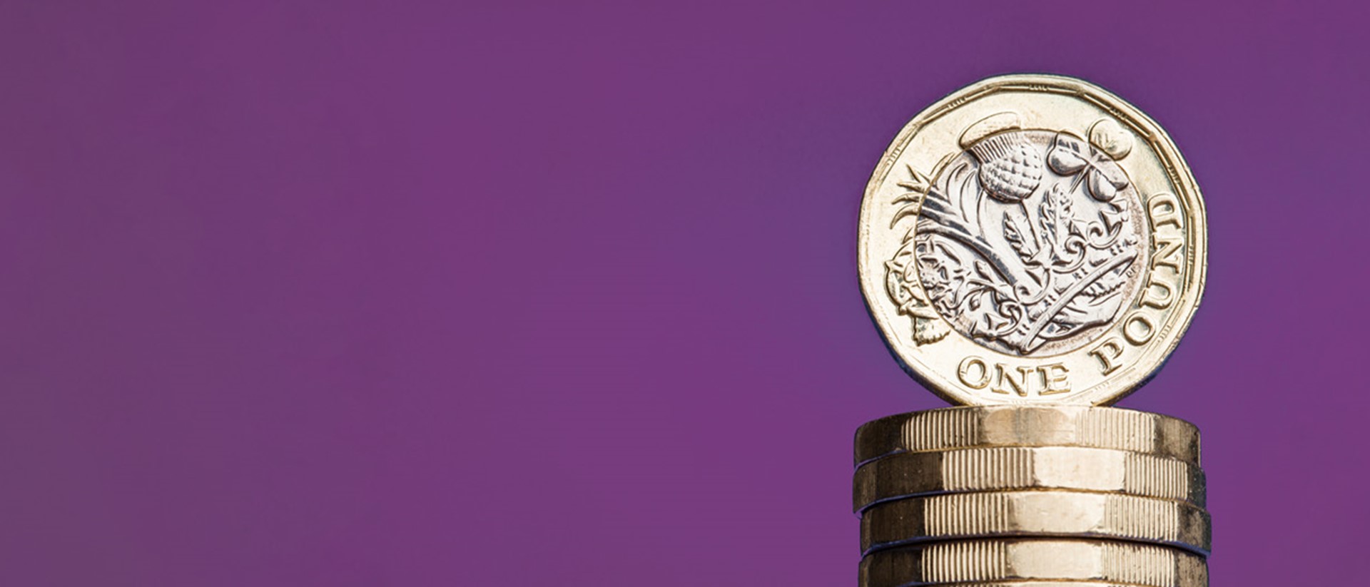 A pound coin stacked on top of other pound coins against a purple background