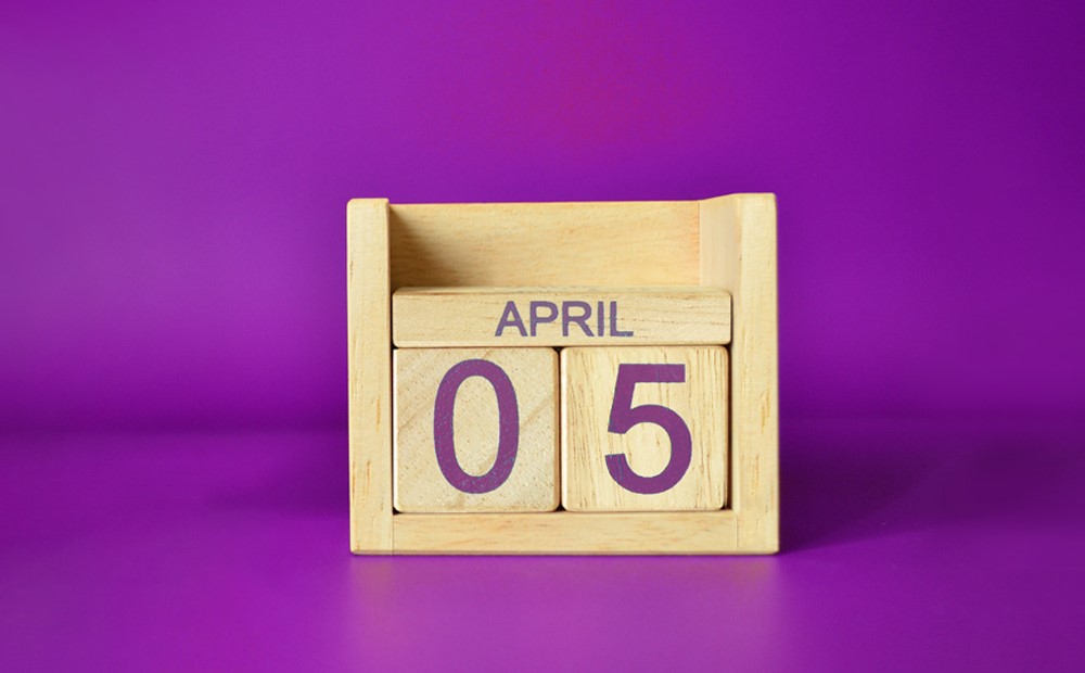 Wooden calendar block with the date of 5th April against a purple background