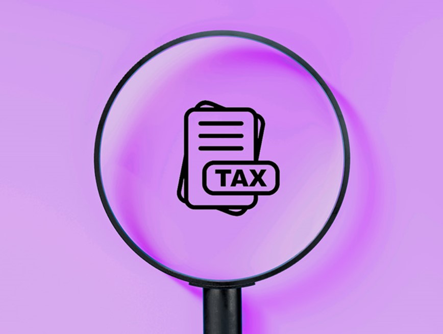 A magnifying glass looking at an icon with the words ‘Tax’ against a purple background