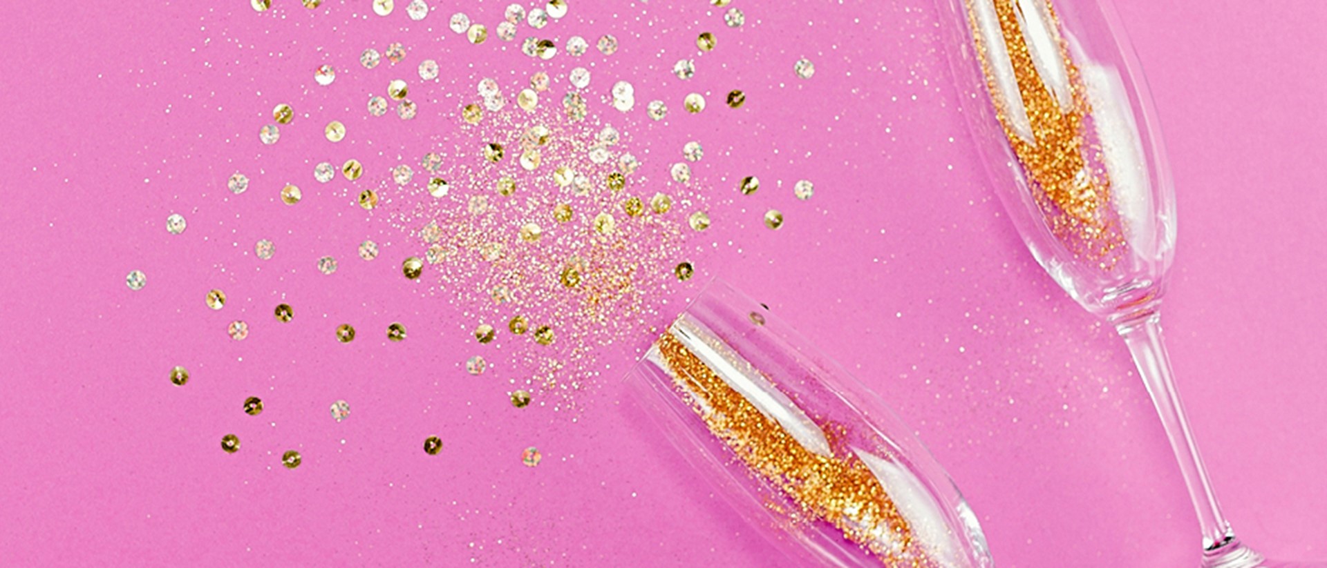 Image of two champagnes flutes with glitter on a pink background