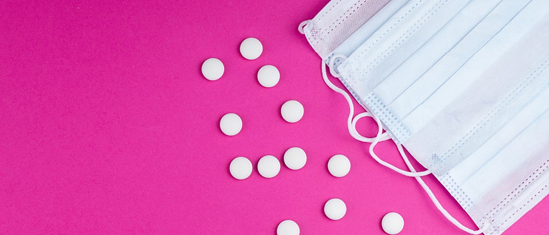 Image of a white surgical mask and pills on a pink background