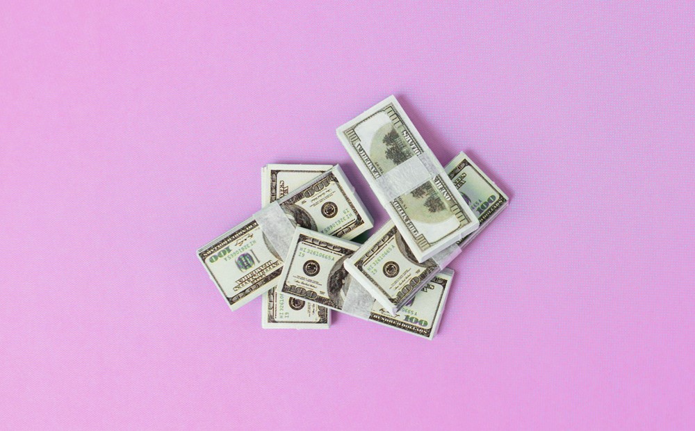 A stack of American dollar bills against a light pink background