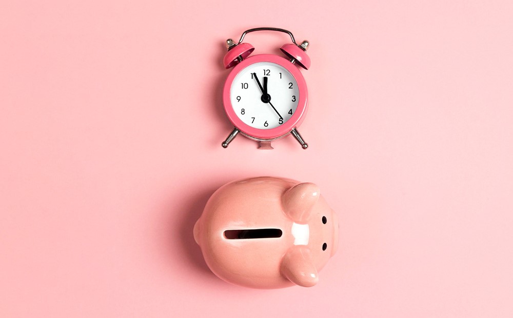 A pink alarm clock and a pink piggy bank against a pink background