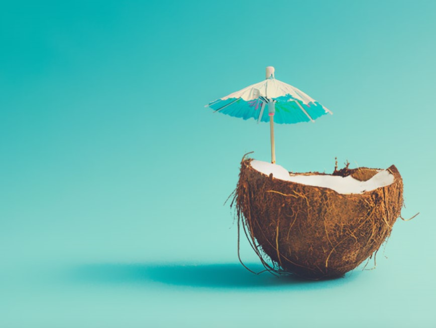 Image of a coconut with a cocktail umbrella on a teal background