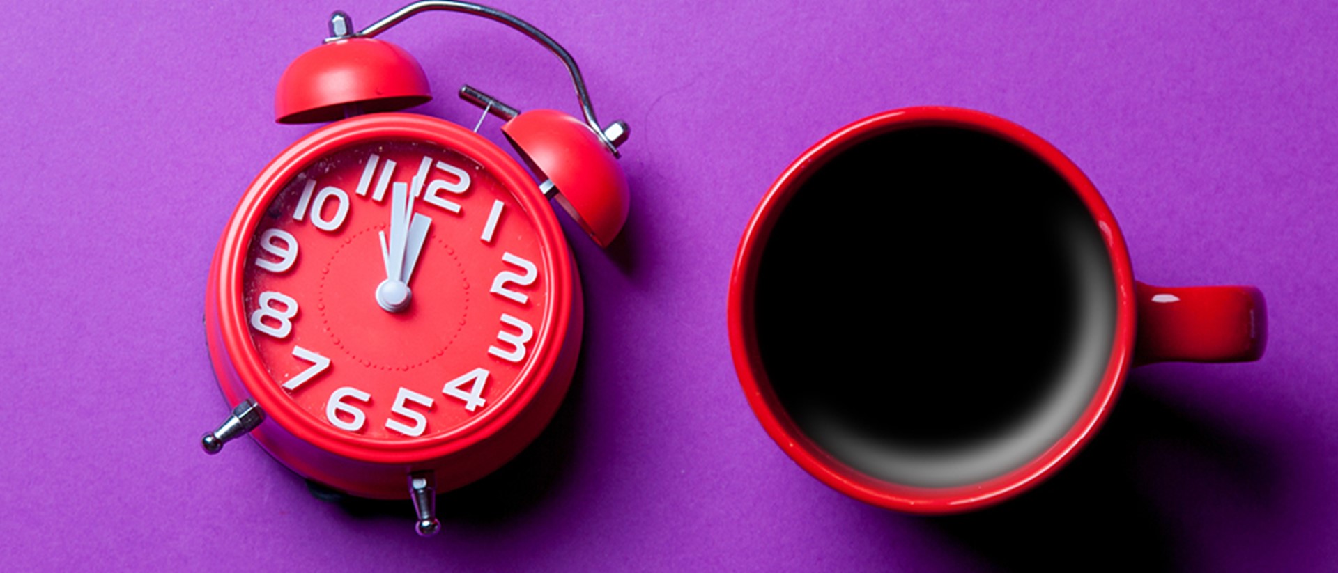 Top down image of red alarm clock and a mug of coffee on a purple background