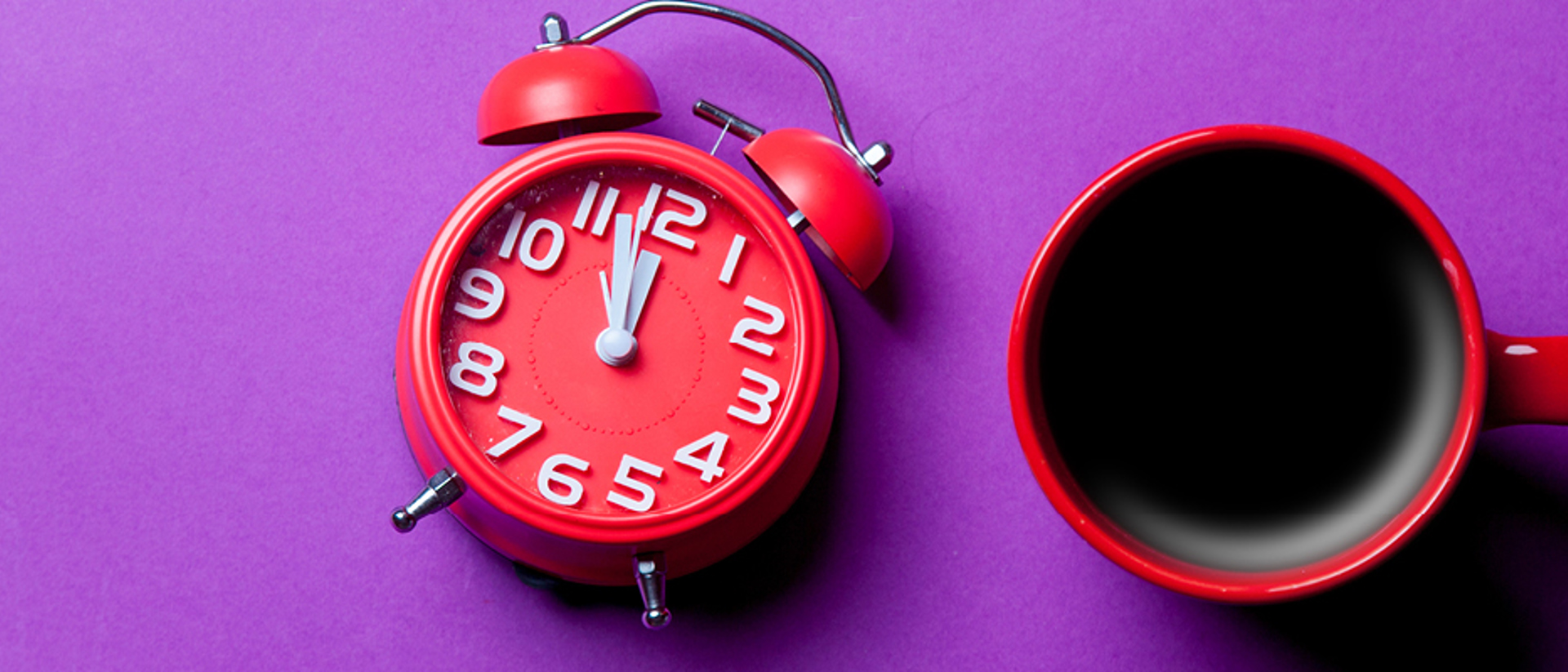 Top down image of red alarm clock and a mug of coffee on a purple background