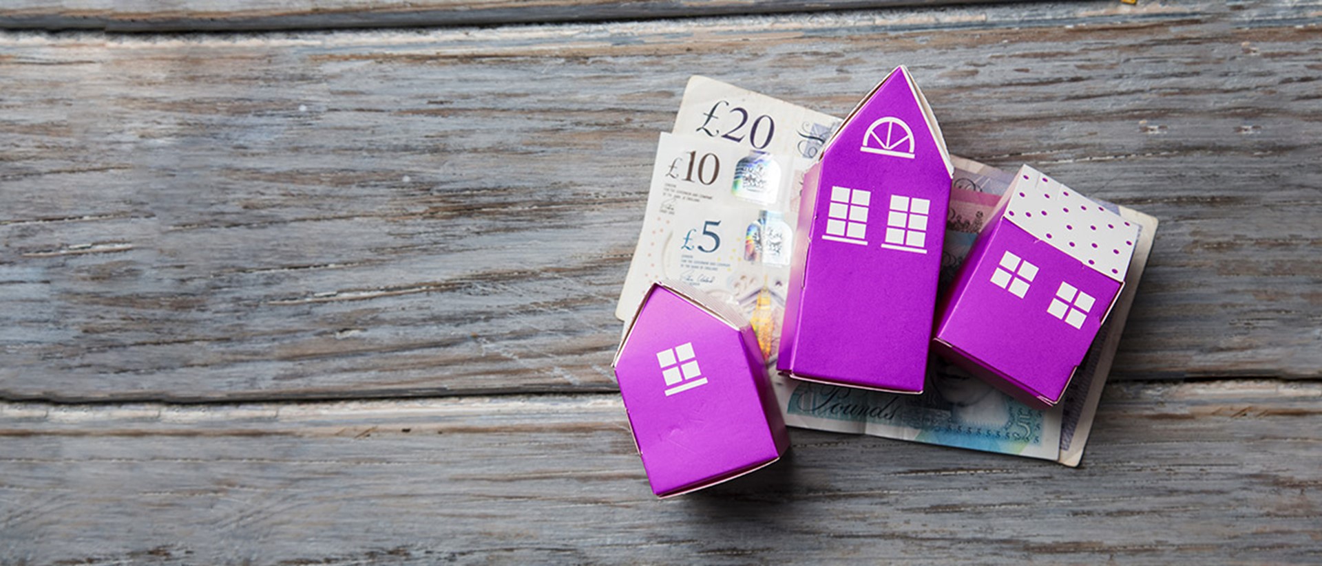 Image of purple cardboard houses on bank notes on top of wooden slabs