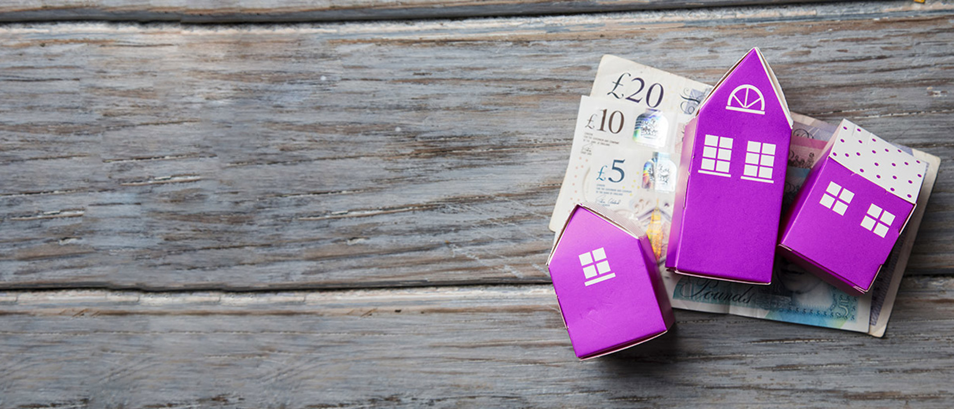 Image of purple cardboard houses on bank notes on top of wooden slabs