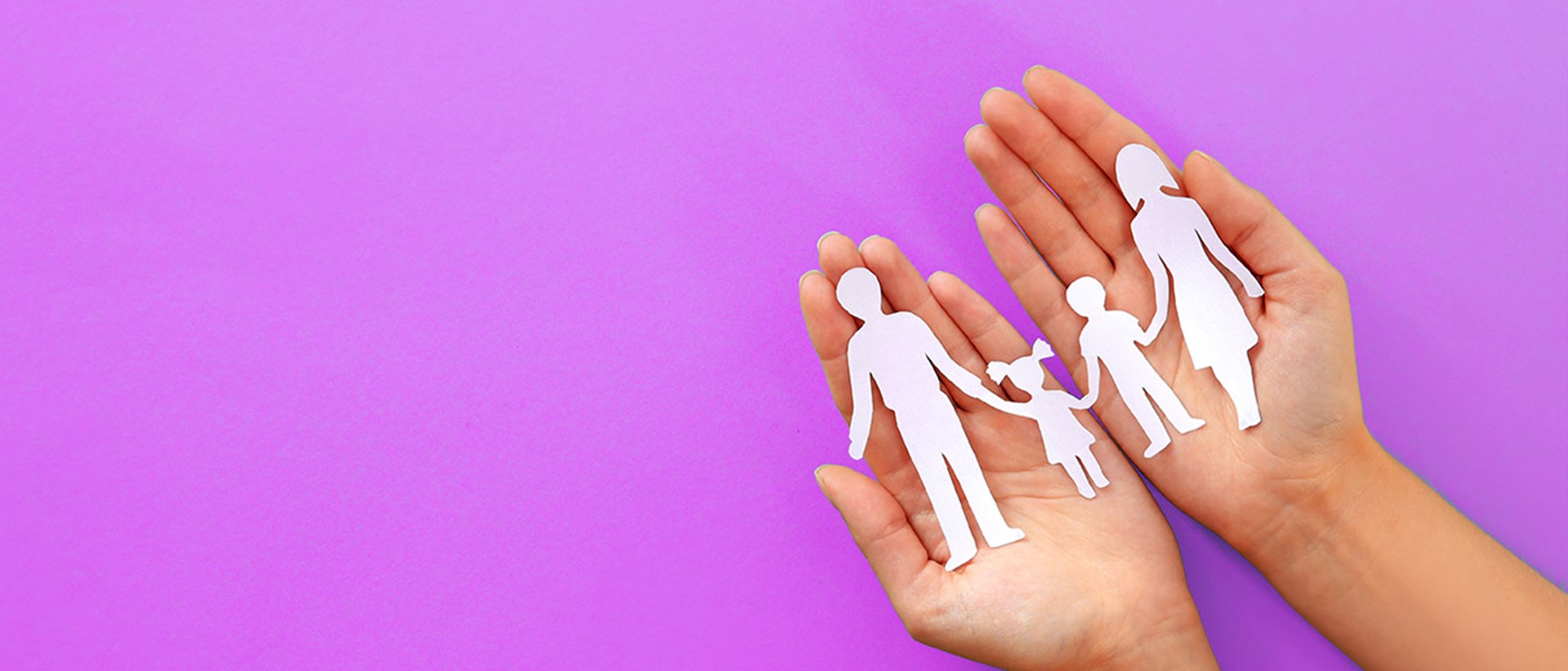 Image of a paper cutout in the shape of a family within a pair of hands on a purple background