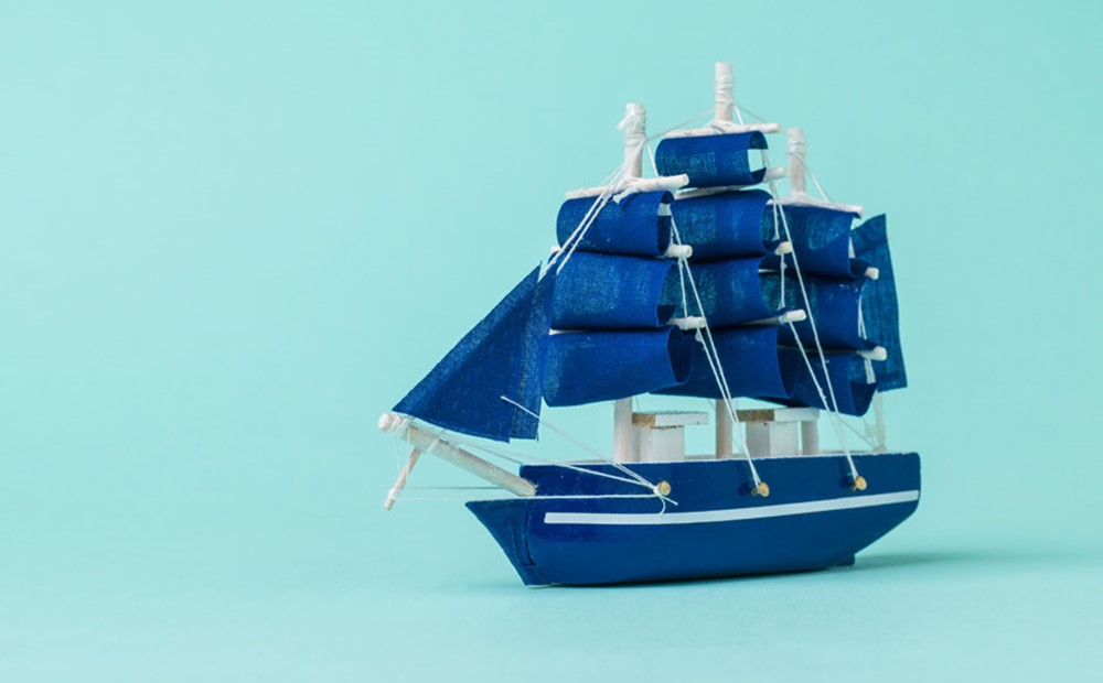 Image of a dark blue sailing ship against a light blue background 