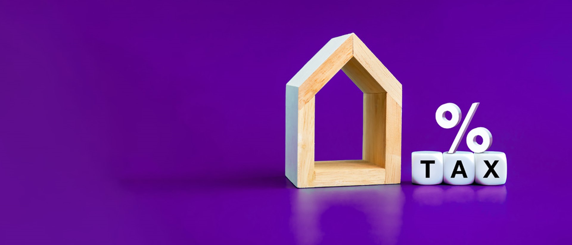 A wooden block shaped as a house, with a percentage symbol on top of dice spelling out TAX, all against a purple background.
