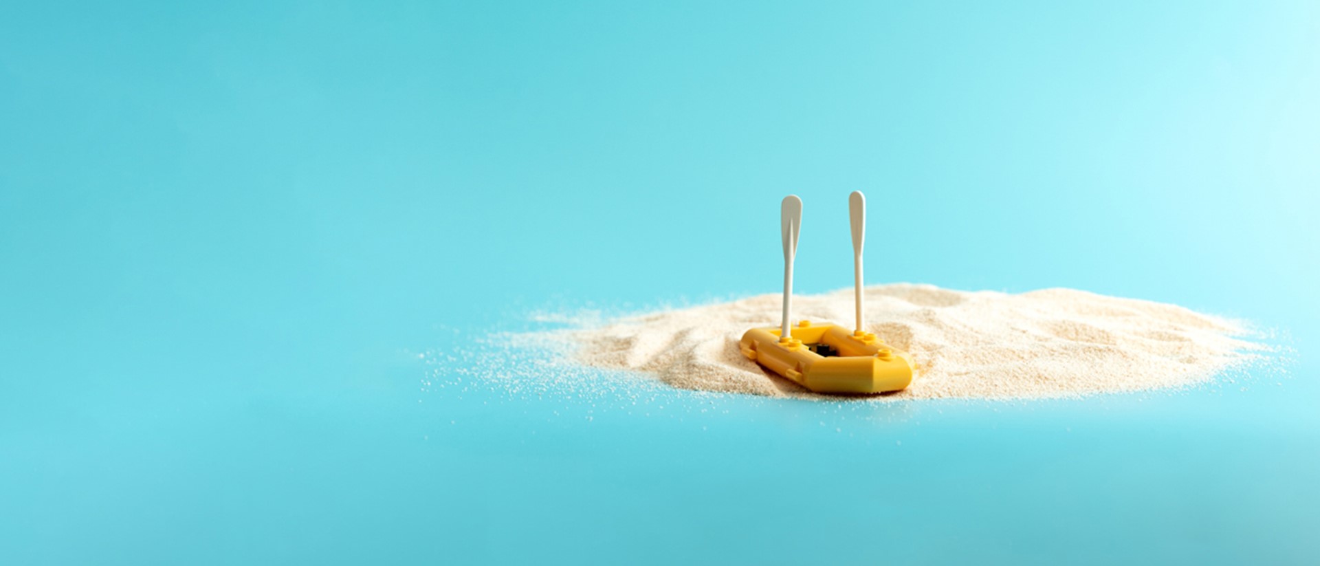 Image of a mini yellow paddle boat on sand against a blue background 