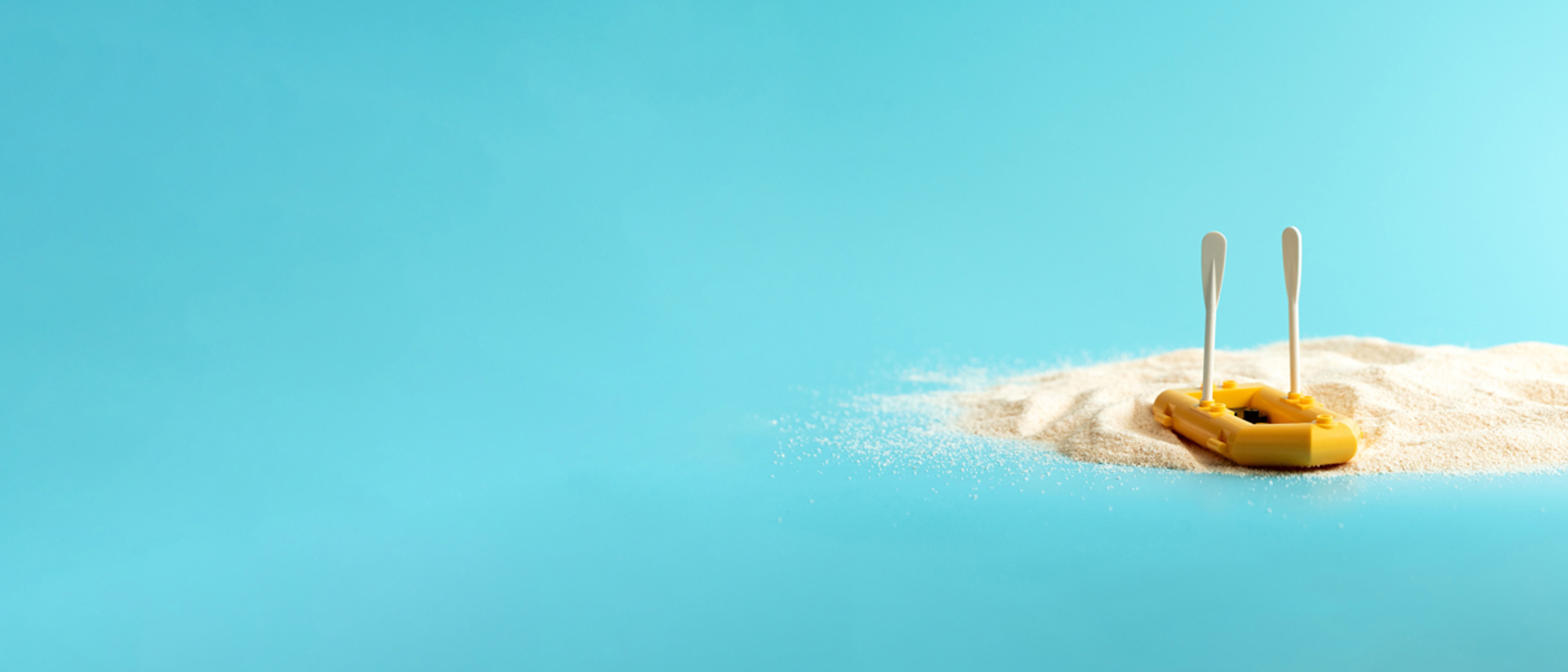 Image of a mini yellow paddle boat on sand against a blue background 