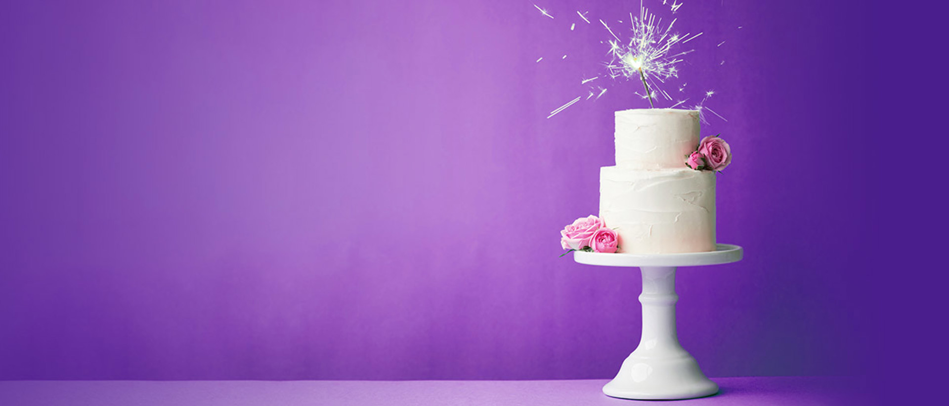 Image of a white wedding cake with a sparkler on a purple background