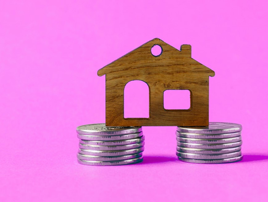 Image of a wooden house on top of two stacks of coins against a purple background