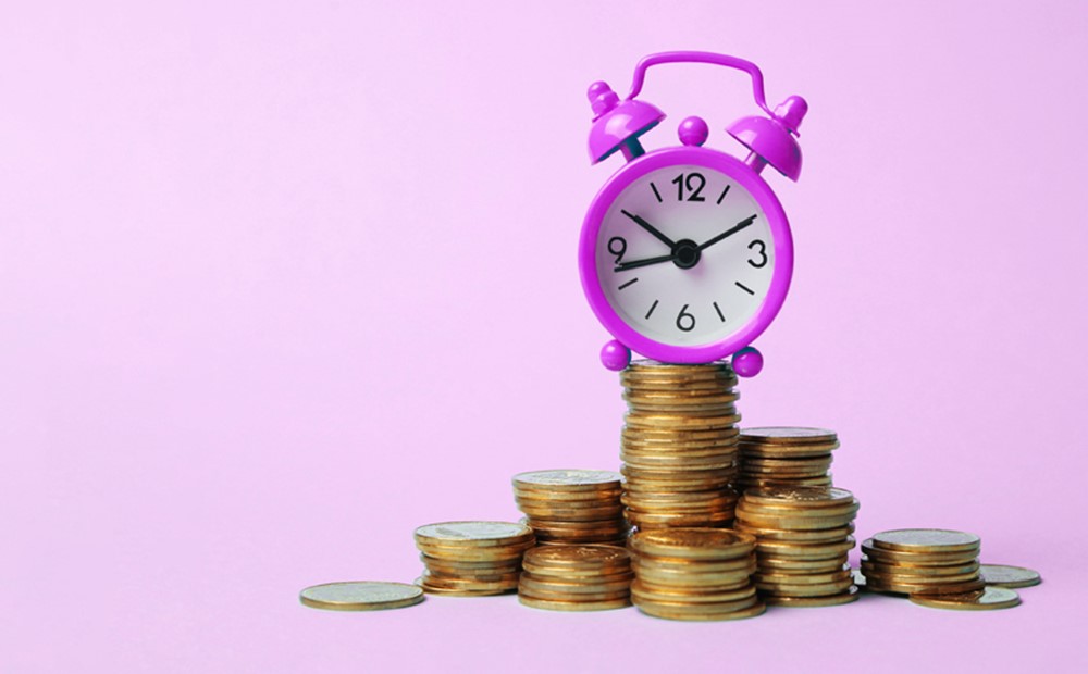 Image of a purple alarm clock sat on a pile of coins on a purple background
