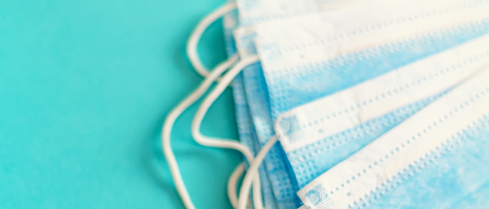 Image of a stack of blue surgical masks on a teal background