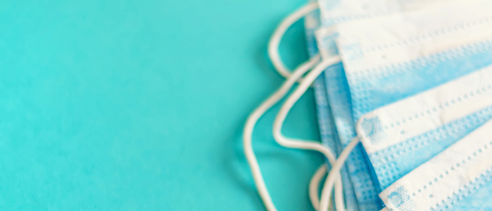 Image of a stack of blue surgical masks on a teal background