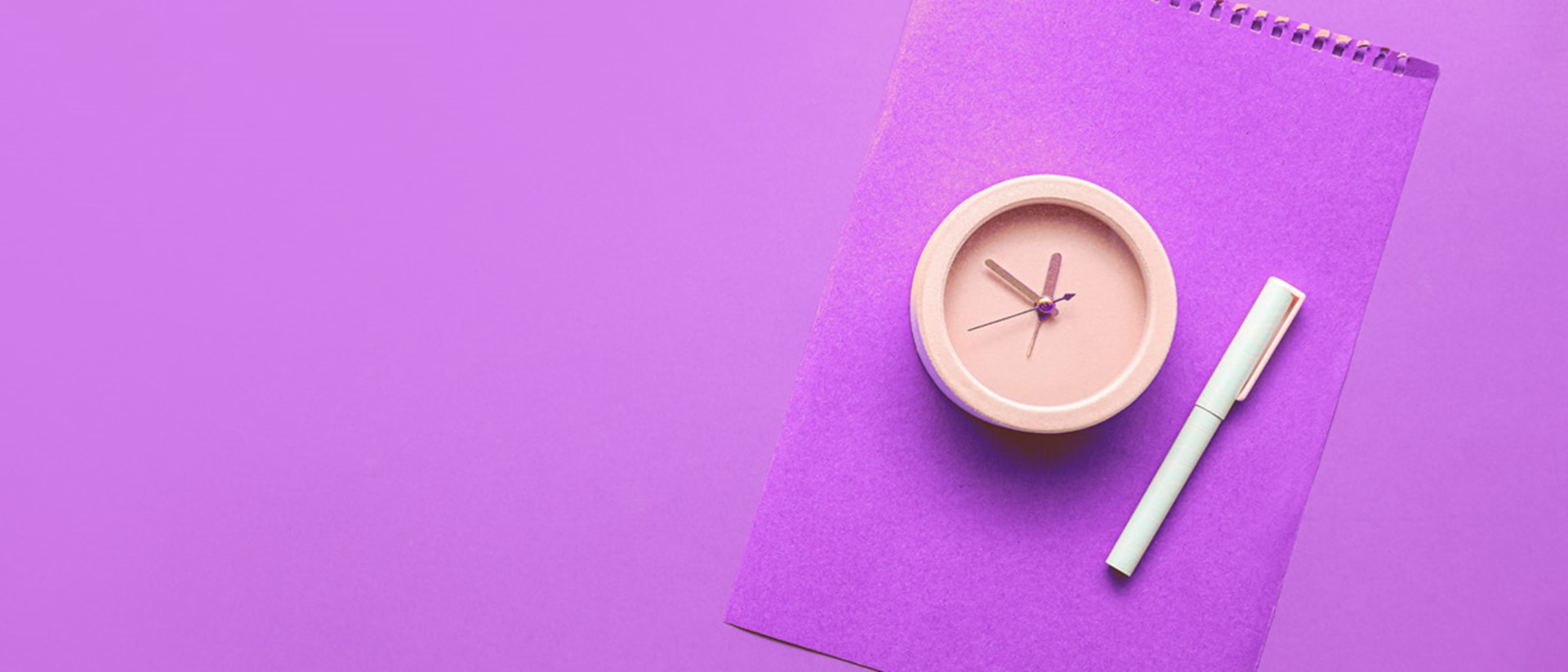 A peach coloured clock and a white pen on top of a purple folder against a purple background