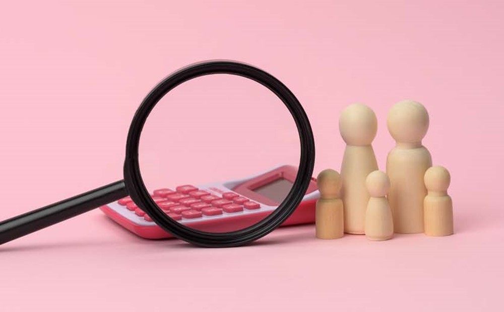Image of a magnifying glass, calculator and wooden figures of people against a pink background