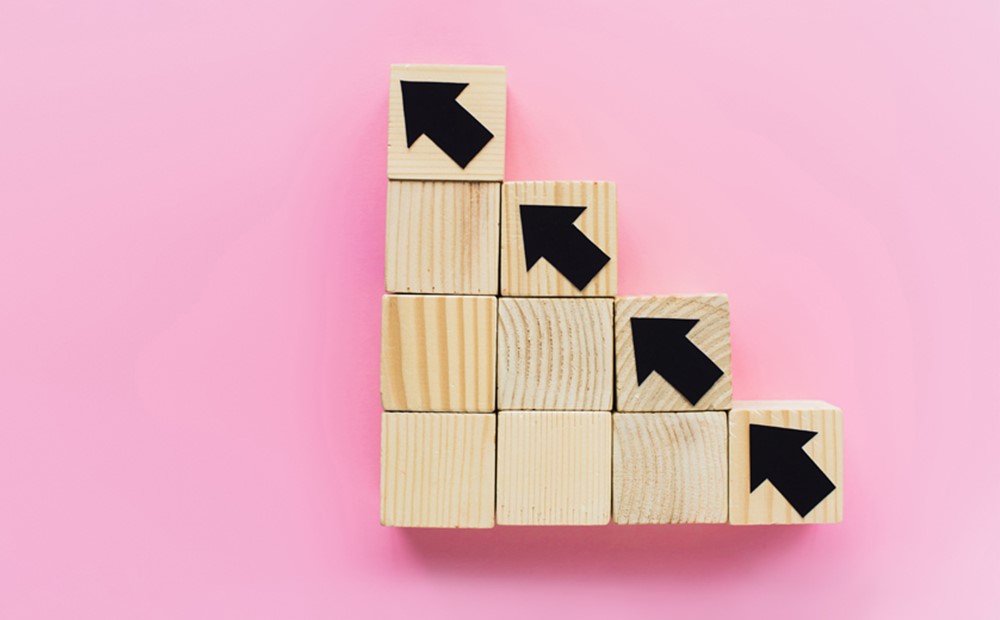 Image of wooden blocks with arrows going diagonally against a pink background