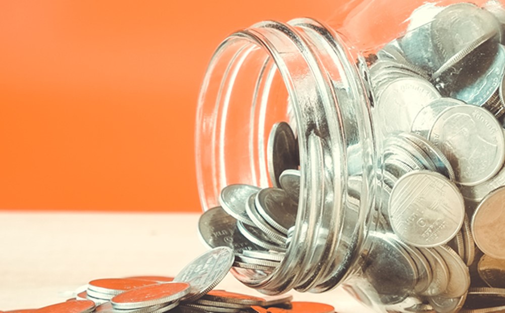 Image of coins flowing our of a glass jar on it's side on an orange background